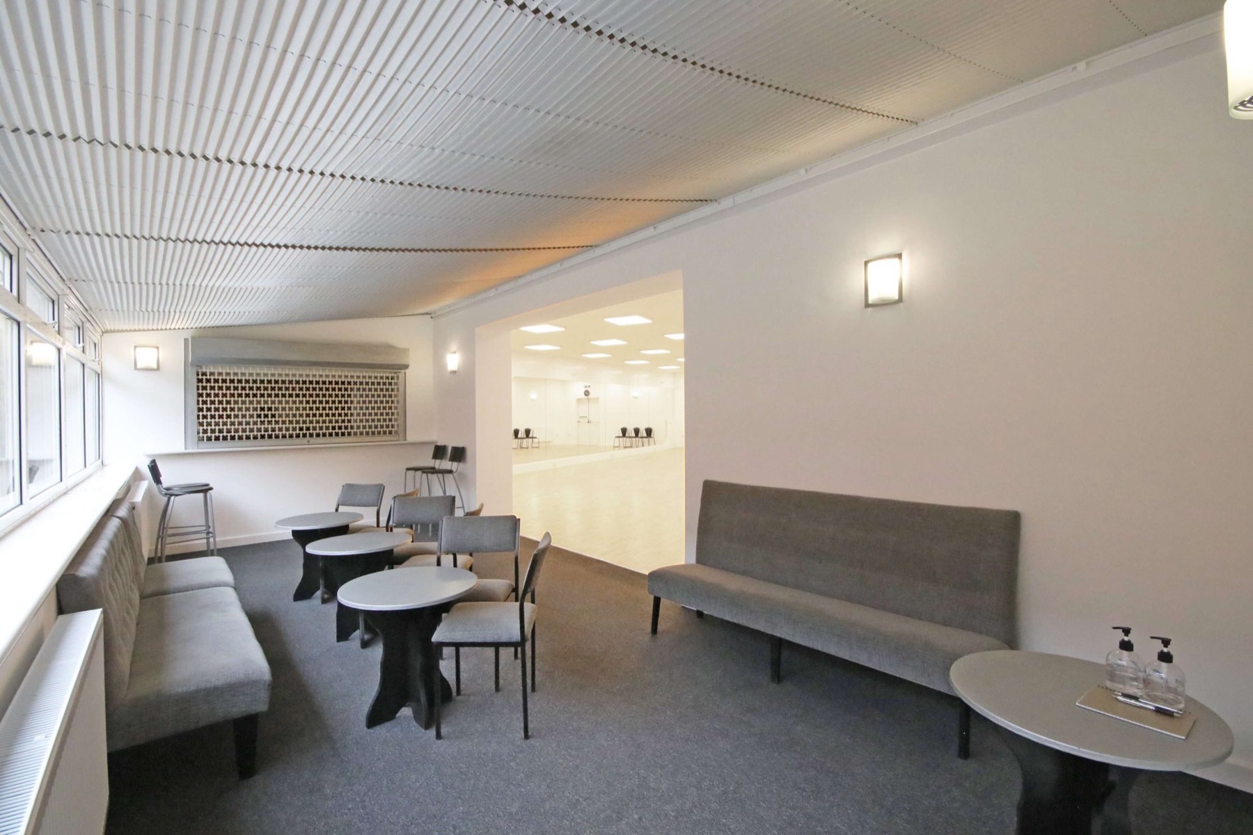The carpeted lounge with seating and tables, looking through the doors to the bright studio floor