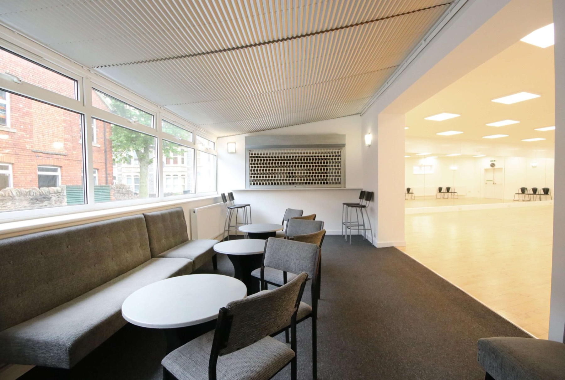 The lounge with a long banquette, round tables and bar stools, the studio visible beyond